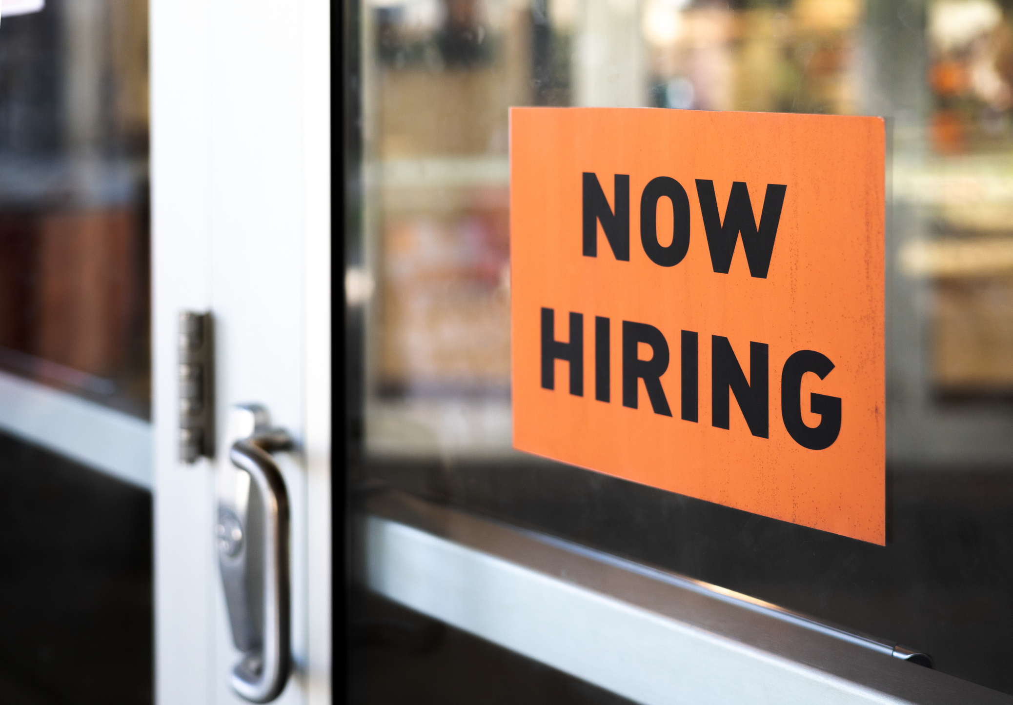 Sign on a door that reads "Now Hiring."