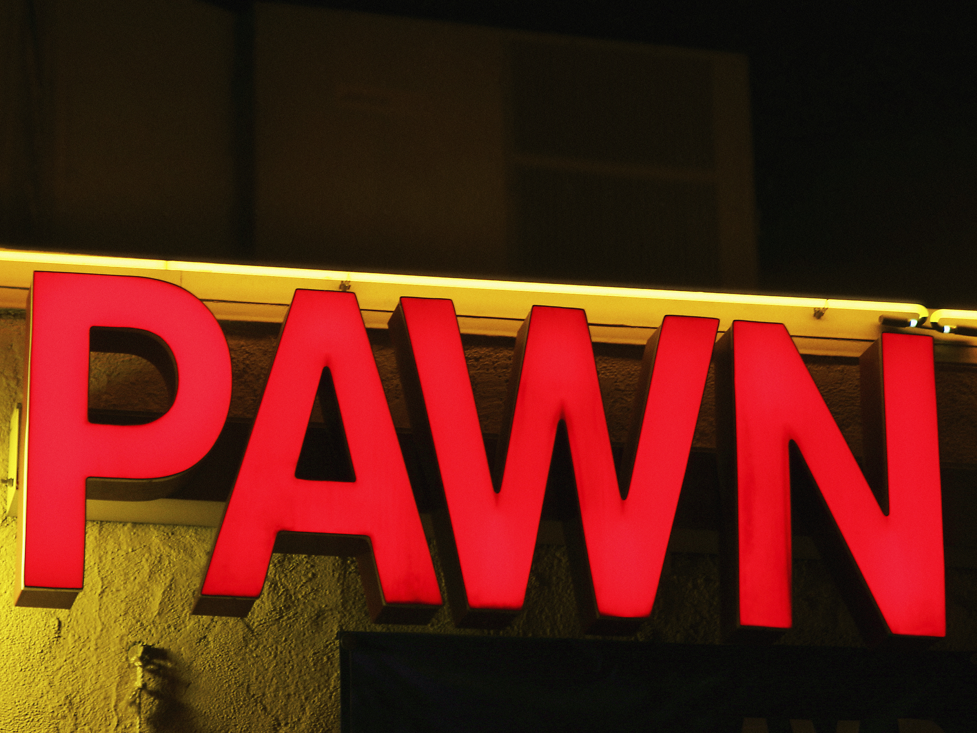 Large red sign displaying the word “PAWN” illuminated at night, likely indicating a pawnshop location