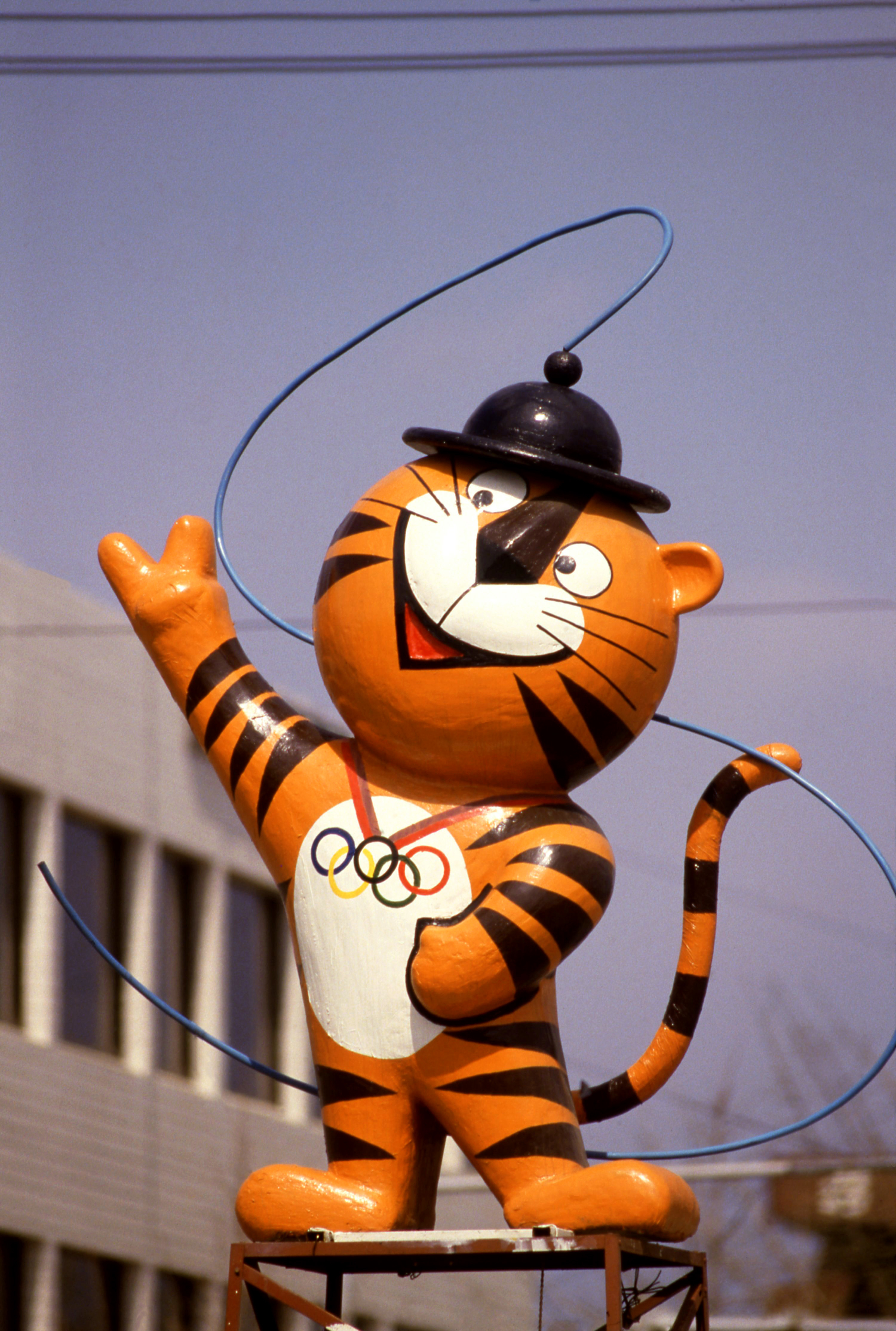 Hodori, the friendly tiger mascot of the 1988 Seoul Olympic Games, waves while wearing an Olympic rings necklace and a traditional Korean hat