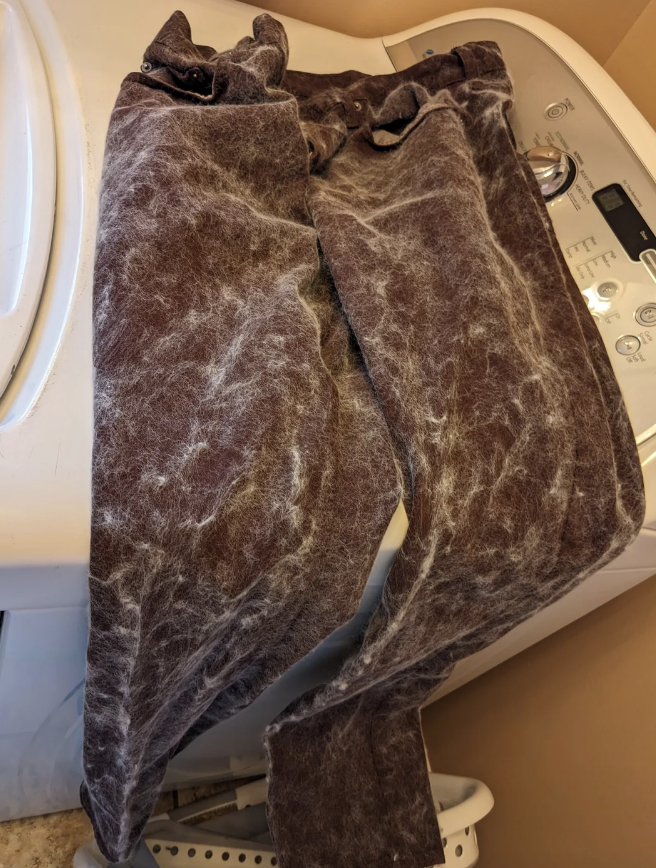 A pair of dark pants covered in pet hair lies on top of a washing machine