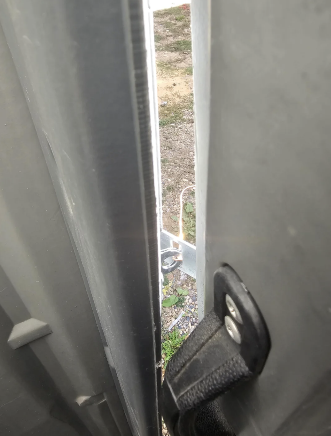 View between slightly open barn doors, looking outside at a metallic latch and gravel ground