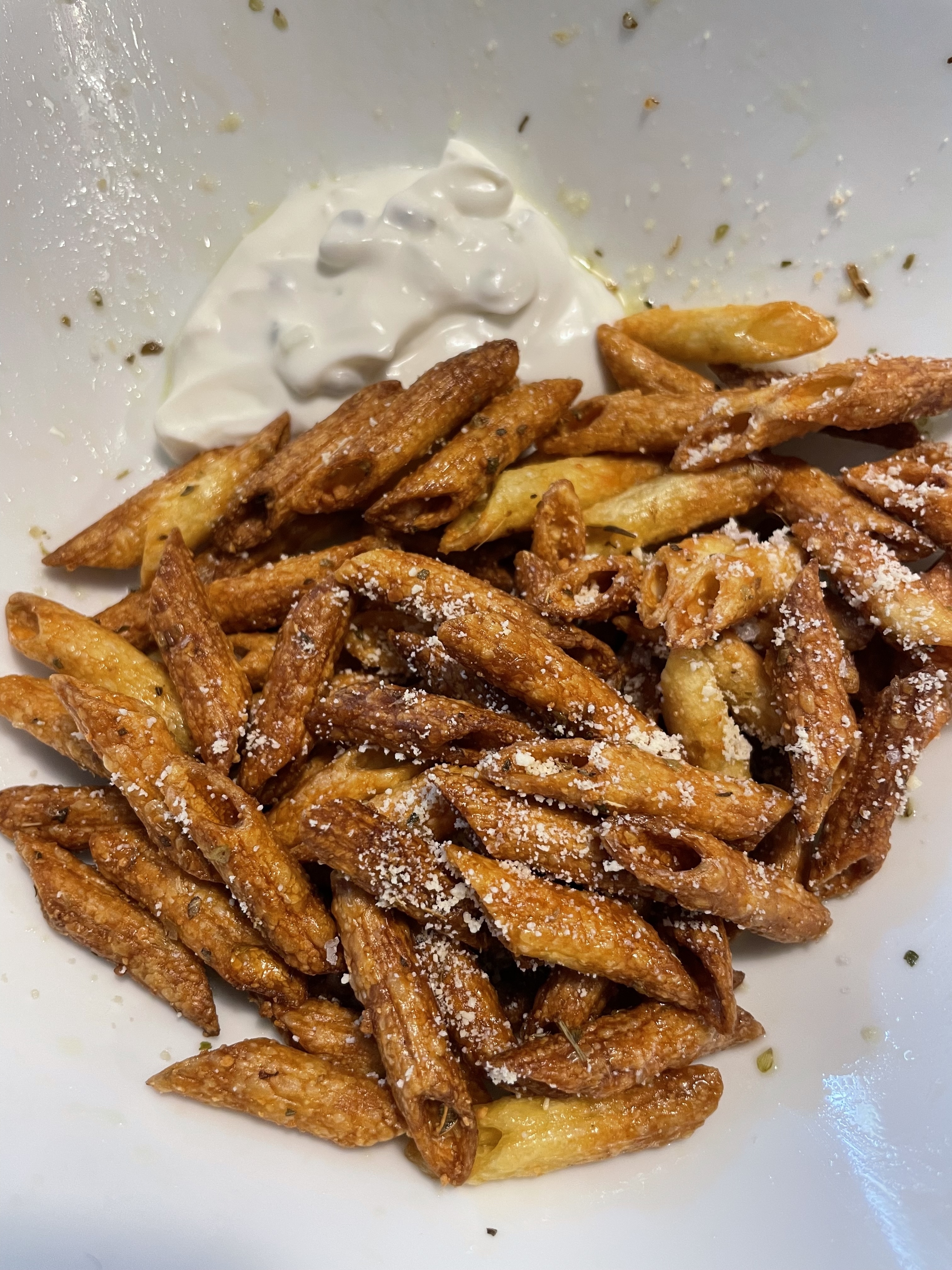 A white bowl filled with crispy pasta chips, topped with grated cheese, served with a side of dip