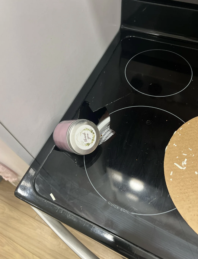 A small jar lies on its side, crushed into the corner of a glass stovetop, causing visible damage to the surface