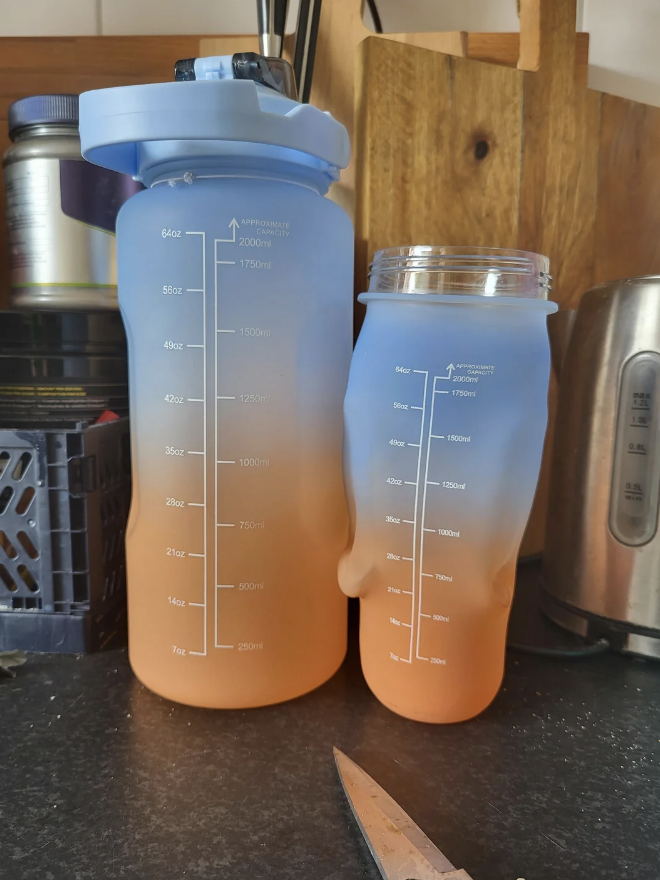 Two semi-transparent water bottles with measurement marks are on a kitchen counter. The bottles appear partially filled and are placed next to a knife and other kitchen items