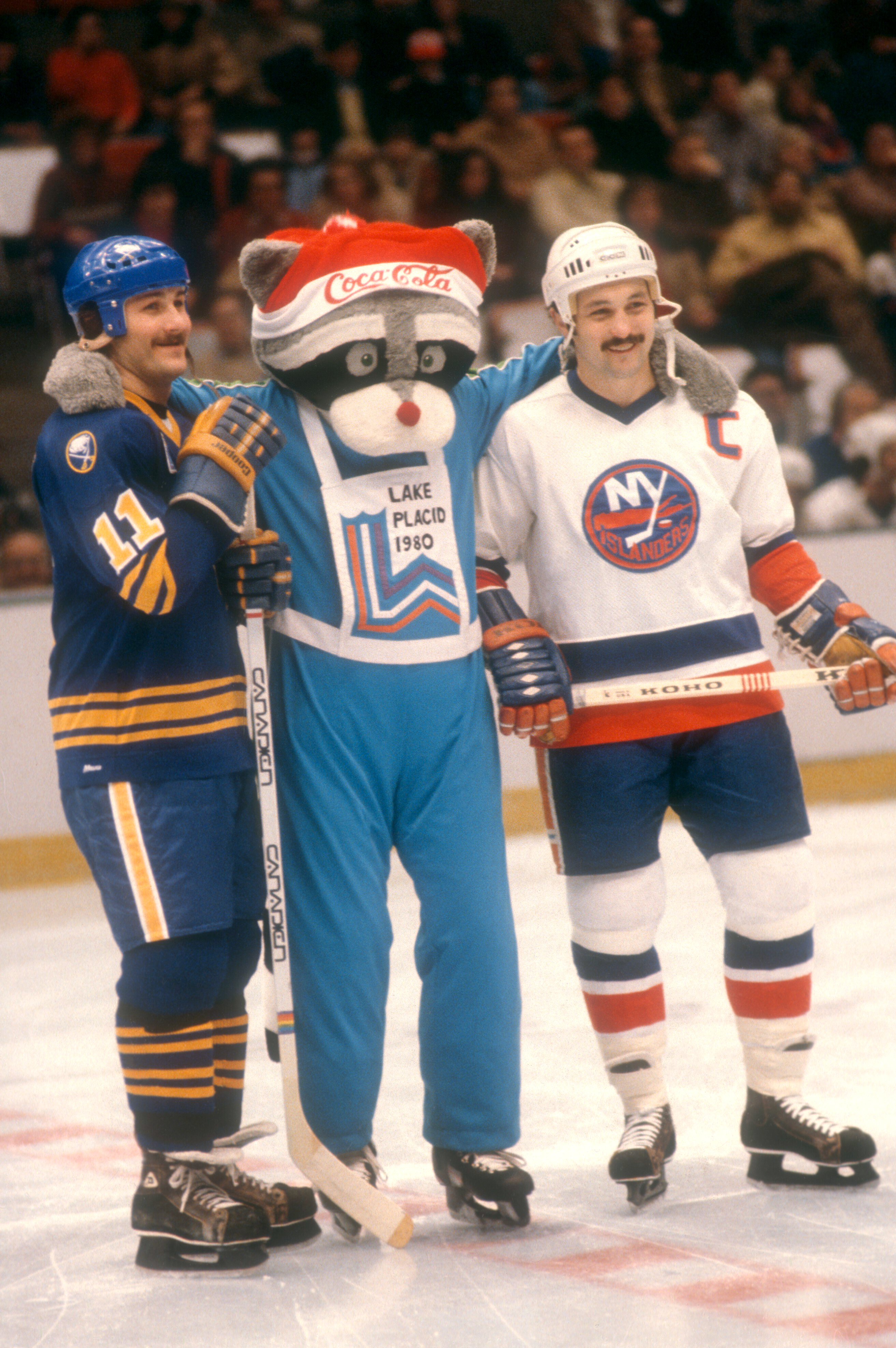 Hockey players Gilbert Perreault and Bryan Trottier stand on the ice with a Lake Placid 1980 Winter Olympics mascot