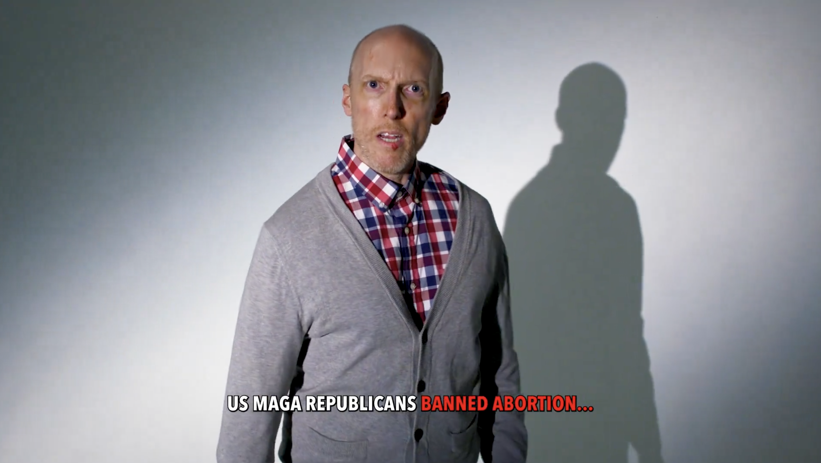 Bald man in a checkered shirt and gray cardigan stands with a concerned expression. The text overlay reads: "US MAGA Republicans BANNED ABORTION…"