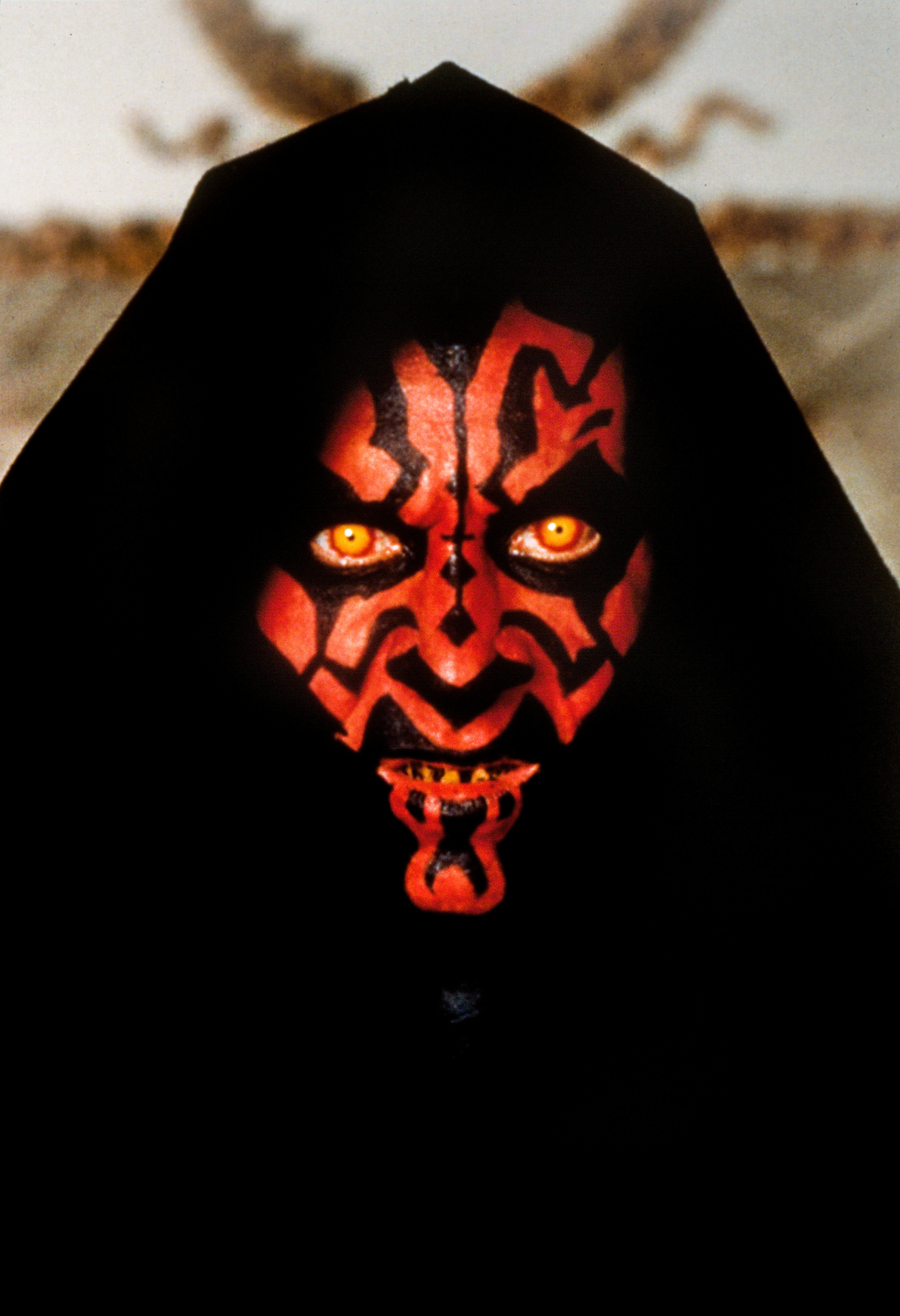 Darth Maul, a character from Star Wars, with black and red facial tattoos, yellow eyes, sharp teeth, and a black hood covering his head