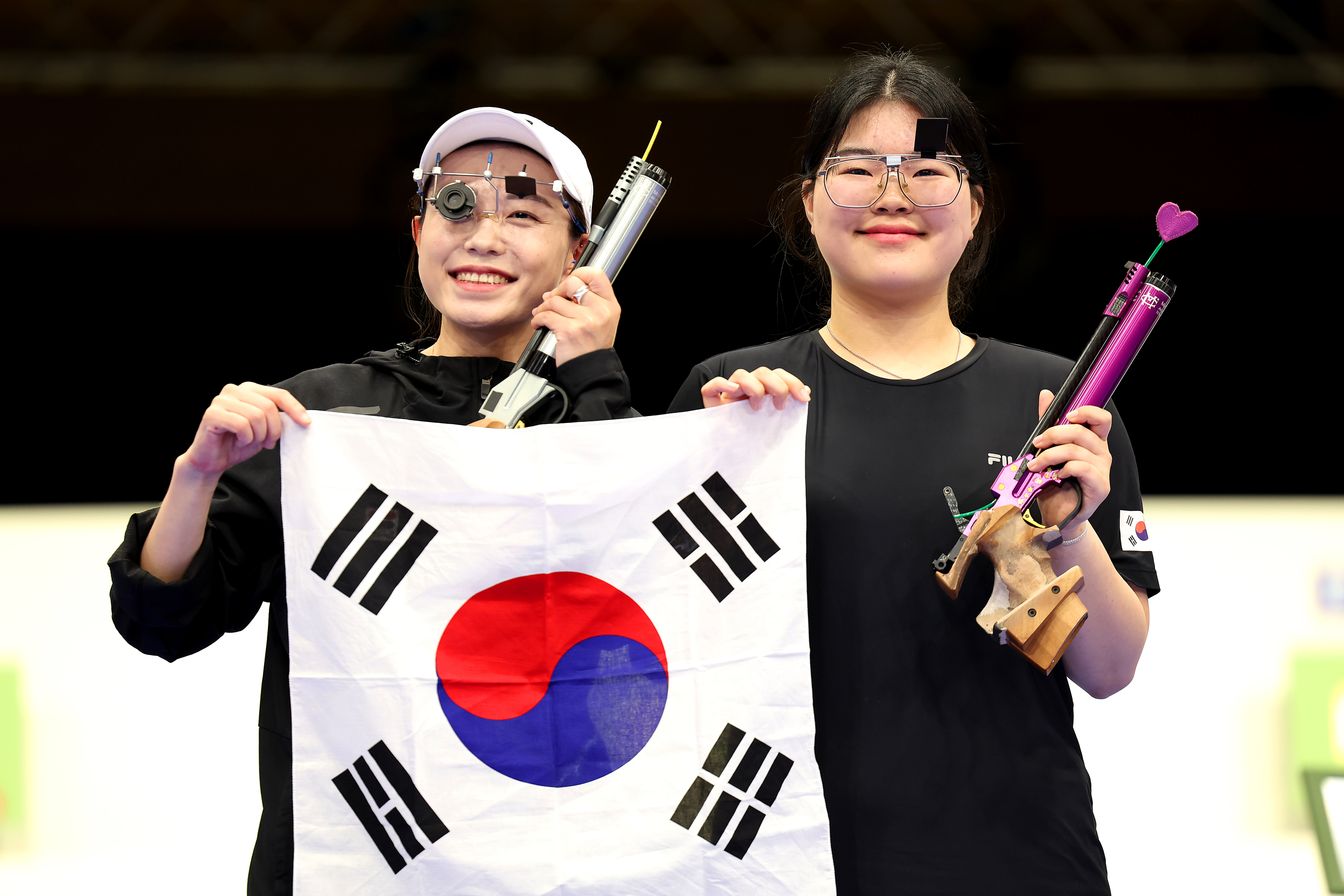 Kim Ye-ji and Oh Ye-jin hold the South Korean flag and their air pistols, smiling after a shooting competition