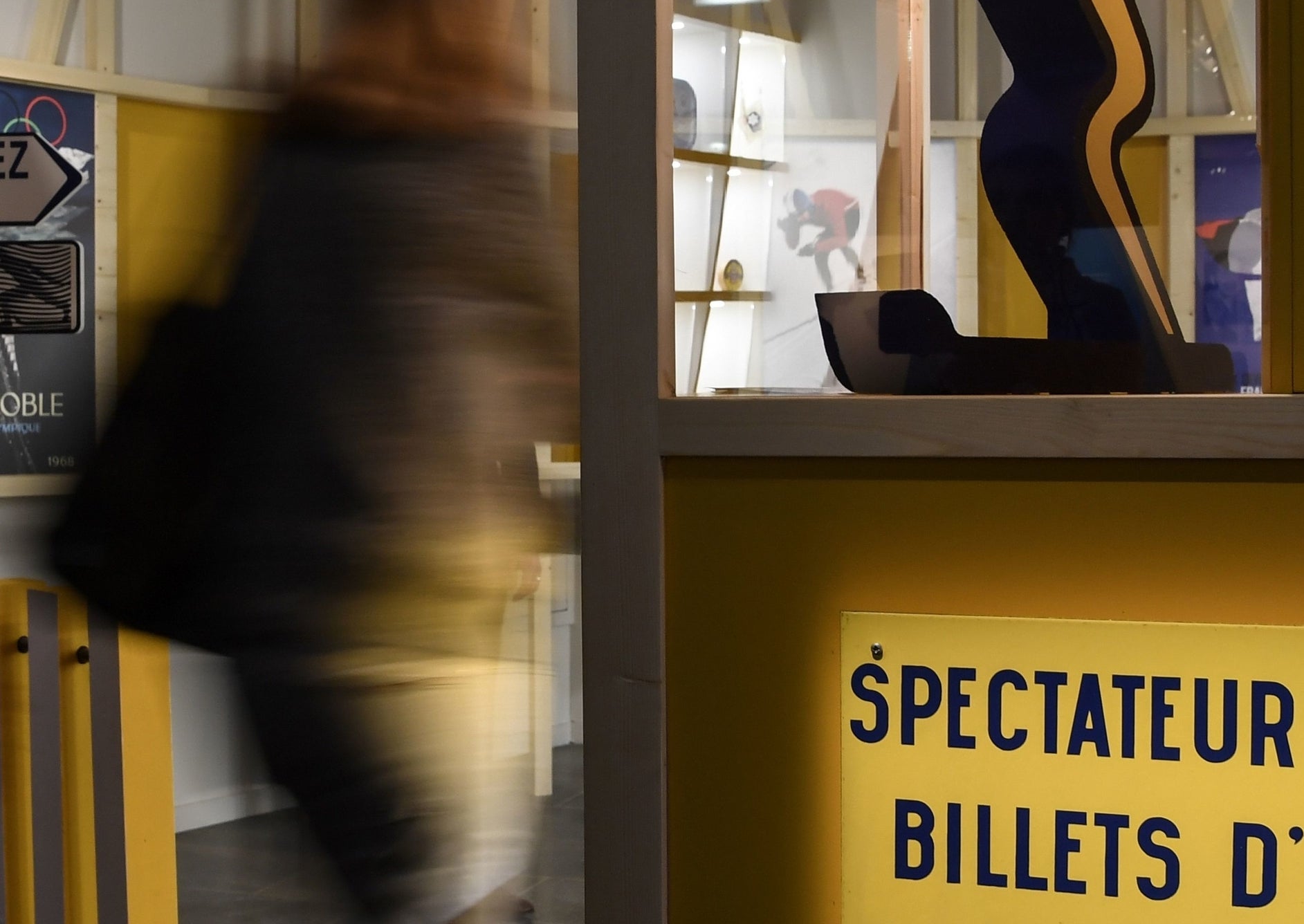 Giant sculpture of a whimsical red-headed figure skiing with a smiling face, viewed through a display case