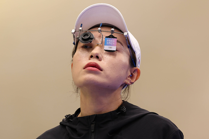 A female athlete wears a white cap and sports vision equipment labeled "Paris 2024 OQP" during a focus-intensive activity