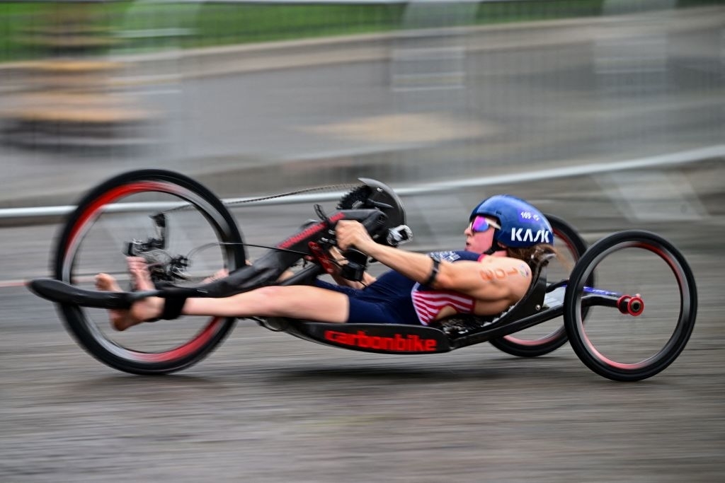 A person in a handcycle race, wearing a helmet and an aerodynamic outfit, is focused on the finish line. The handcycle is labeled &quot;carbonbike.&quot;