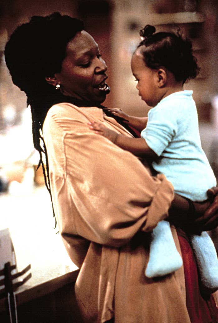 Whoopi Goldberg holds a young toddler, looking at them with a smile
