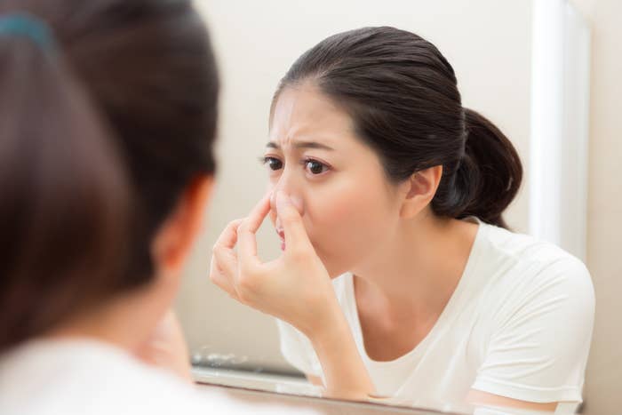 Woman in a white shirt looks in a mirror, concerned and pinching her nose