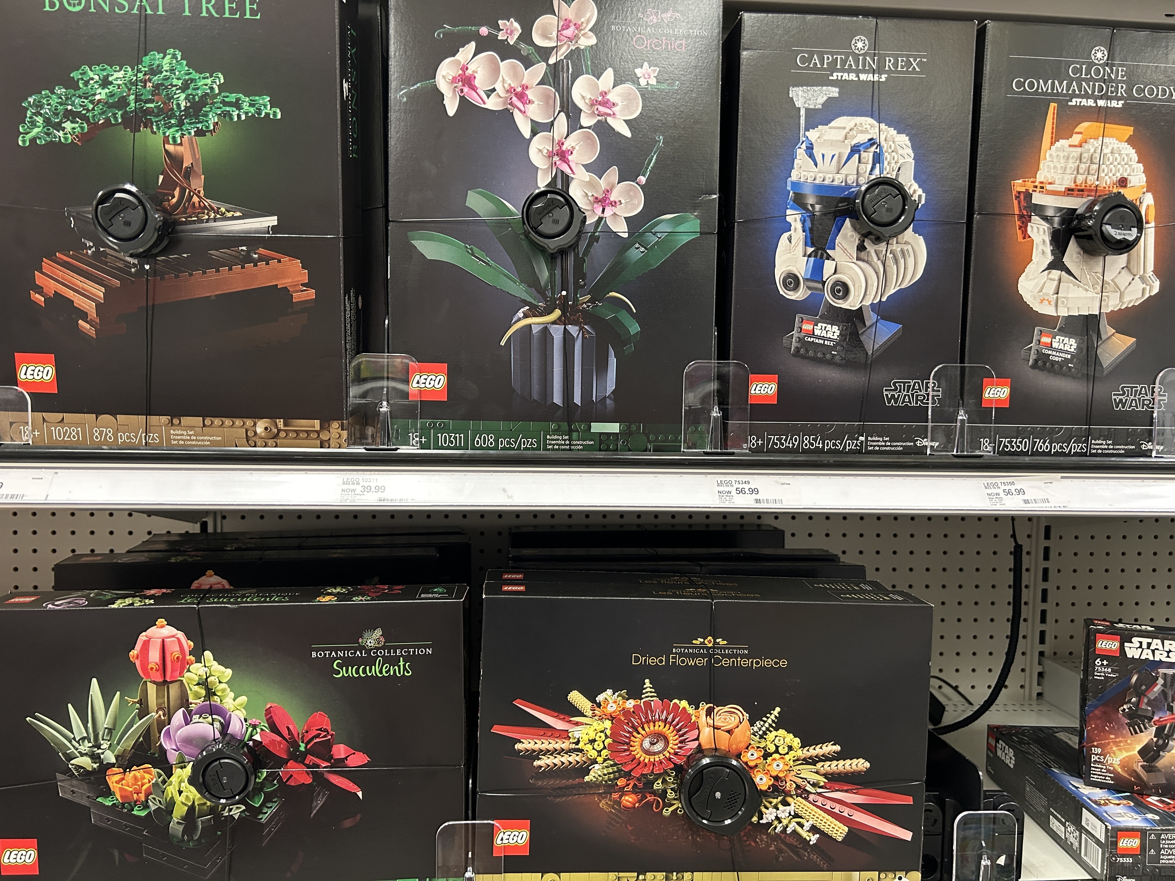 Lego sets on a store shelf, including Bonsai tree, orchid, Captain Rex, Clone Commander Cody, succulent collection, and dried flower centerpiece