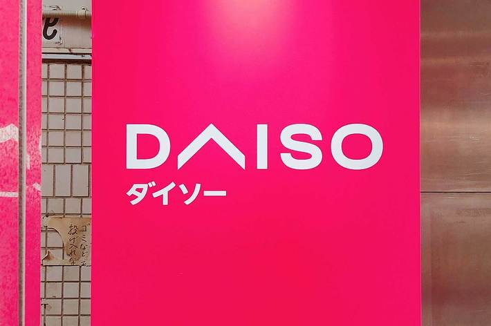 ダイソーの看板。ピンクの背景に白い文字で「ダイソー」と書かれている。