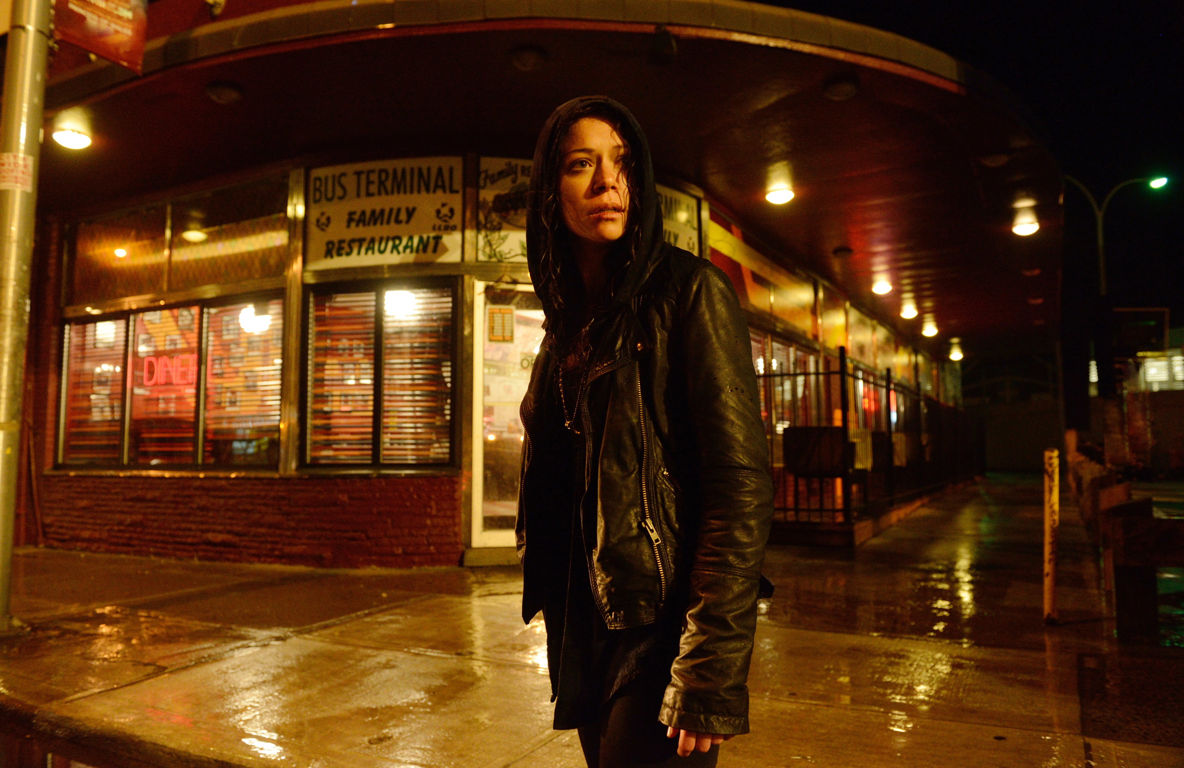 Tatiana Maslany standing on an empty street corner in a leather jacket with the hood up in a scene from "Orphan Black"