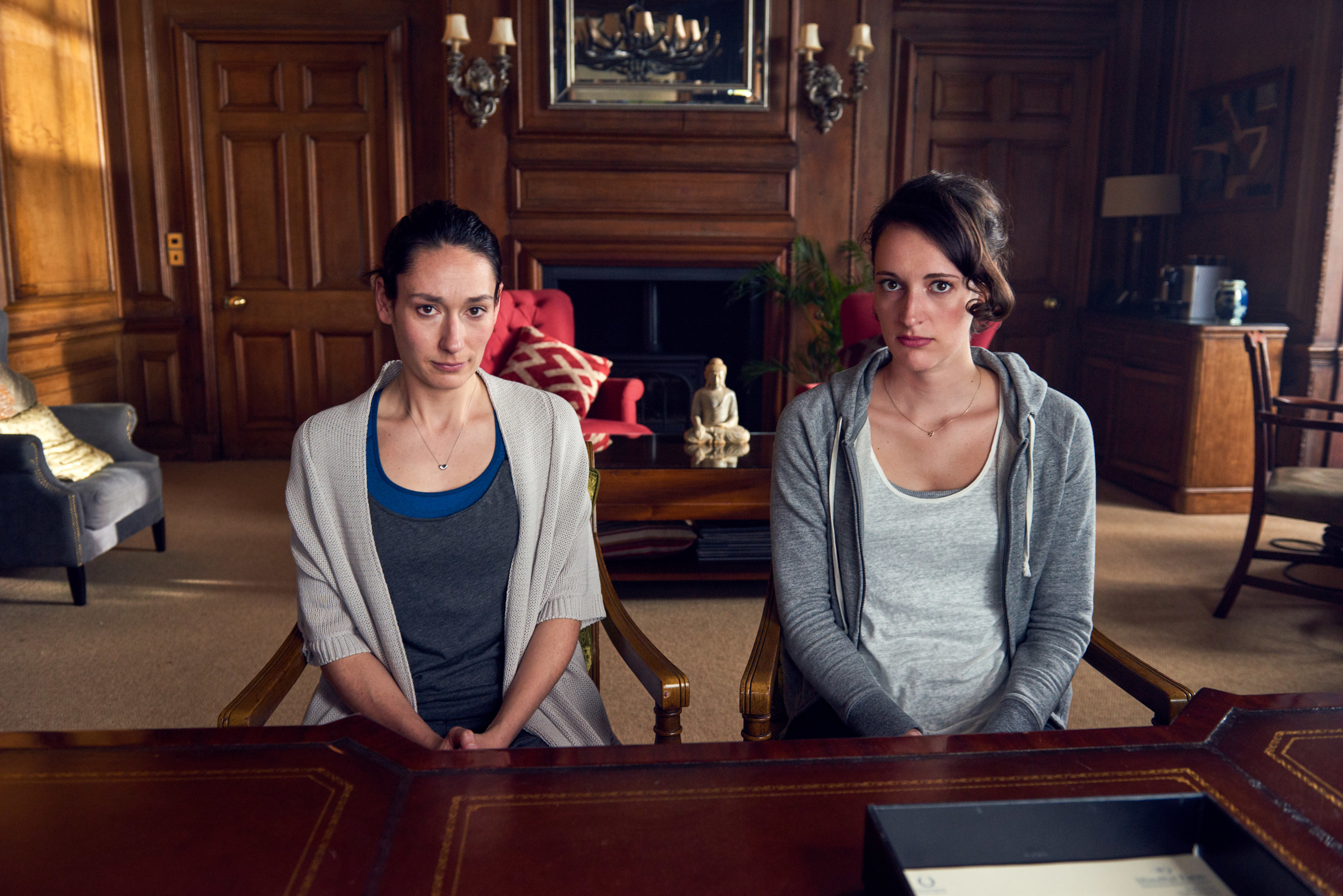 Sian Clifford and Phoebe Waller-Bridge sitting in office charms with wooden arms in a scene from "Fleabag"