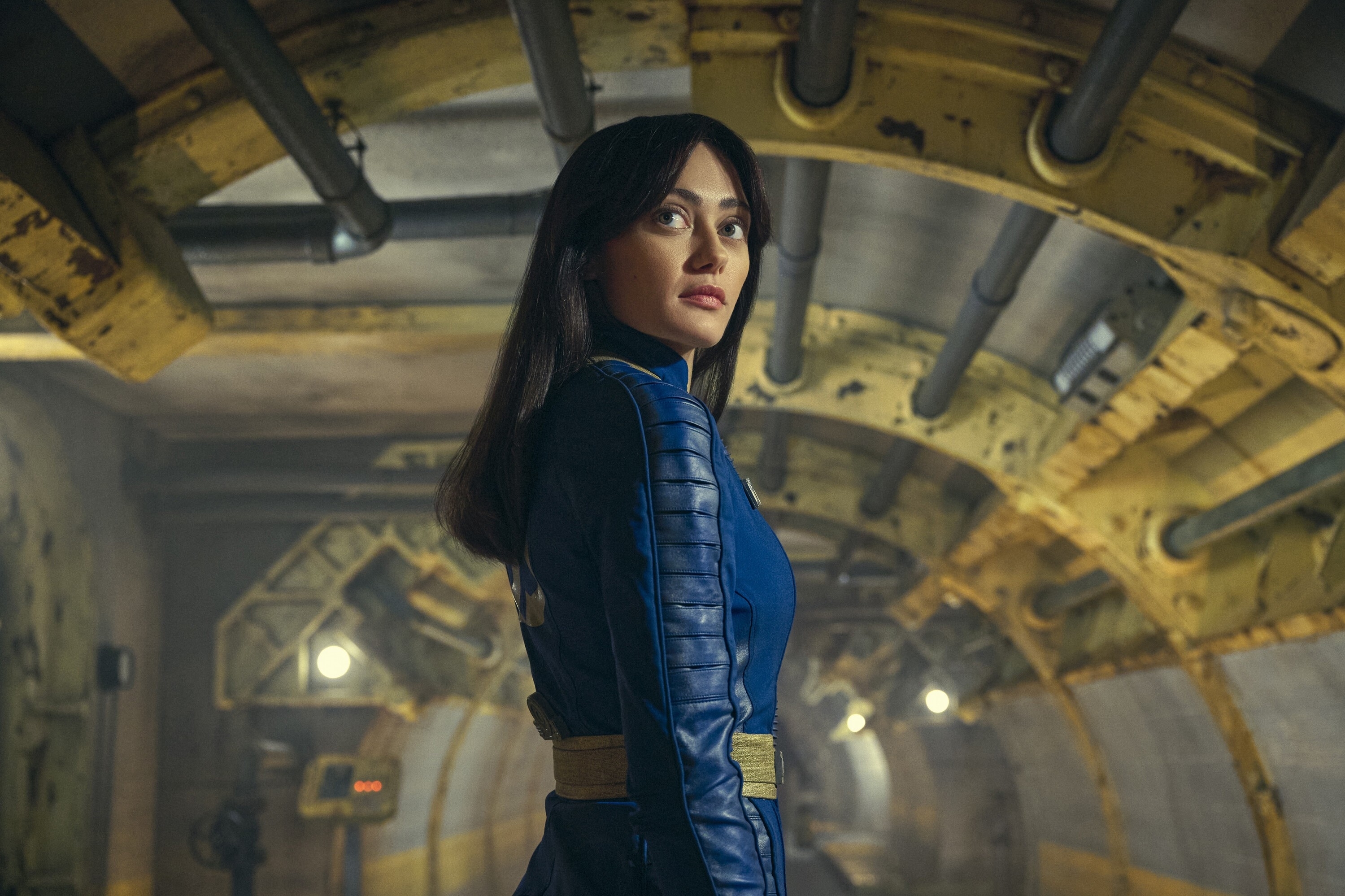 Ella Purnell, in a blue futuristic outfit, stands in an industrial-looking tunnel in a scene from "Fallout"