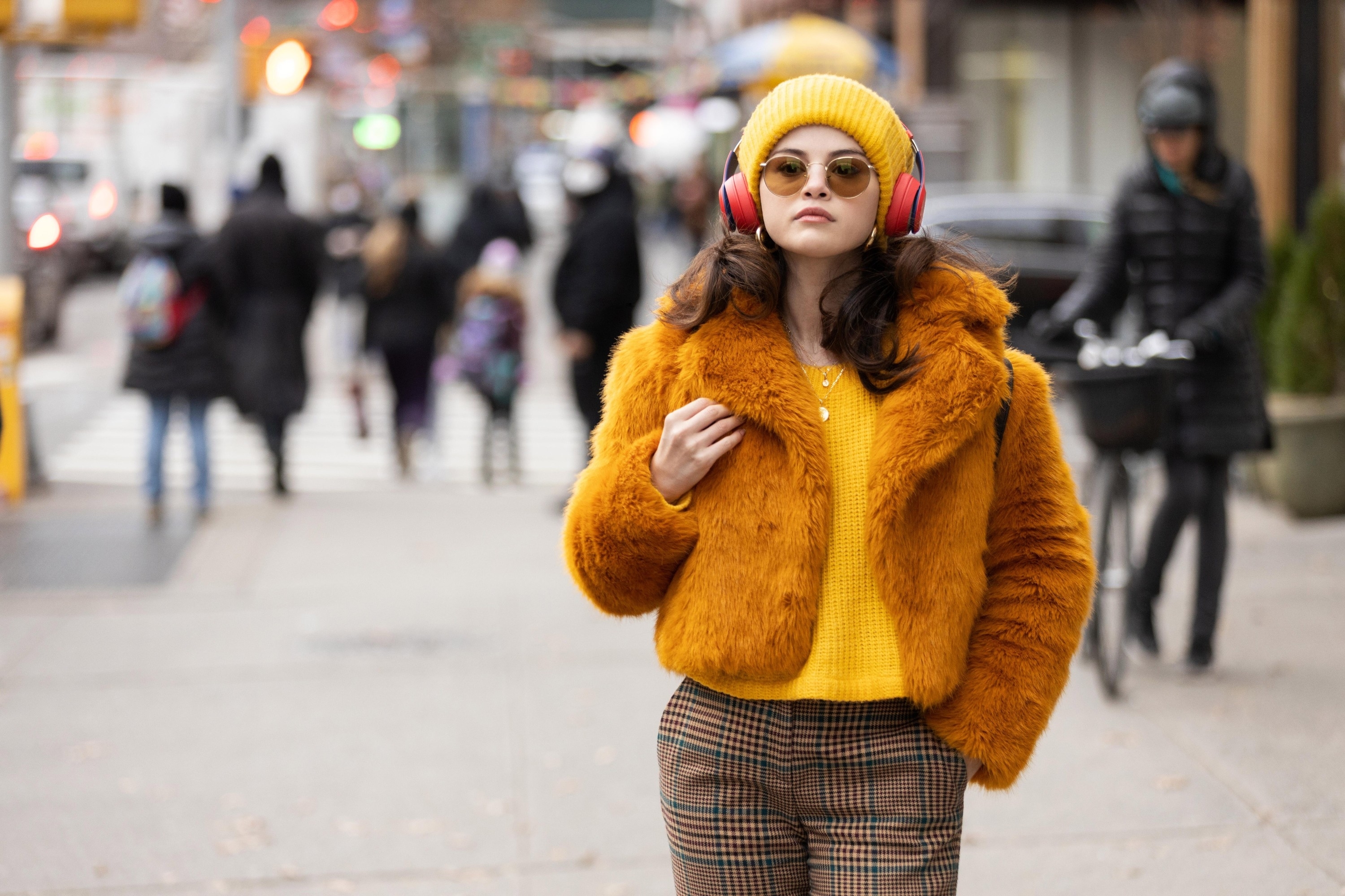 Selena Gomez in a fur jacket, plaid pants, yellow beanie, and shirt in a scene from "Only Murders in the Building"