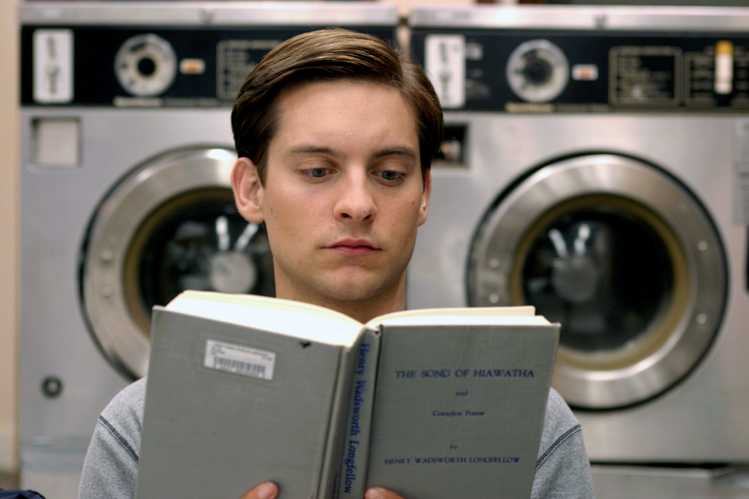 Tobey Maguire is reading &quot;The Song of Hiawatha&quot; in a laundromat with washing machines in the background