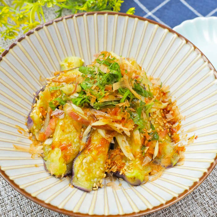 お皿に盛り付けられた焼き茄子の料理。トッピングに刻んだ大葉と鰹節が添えられている。