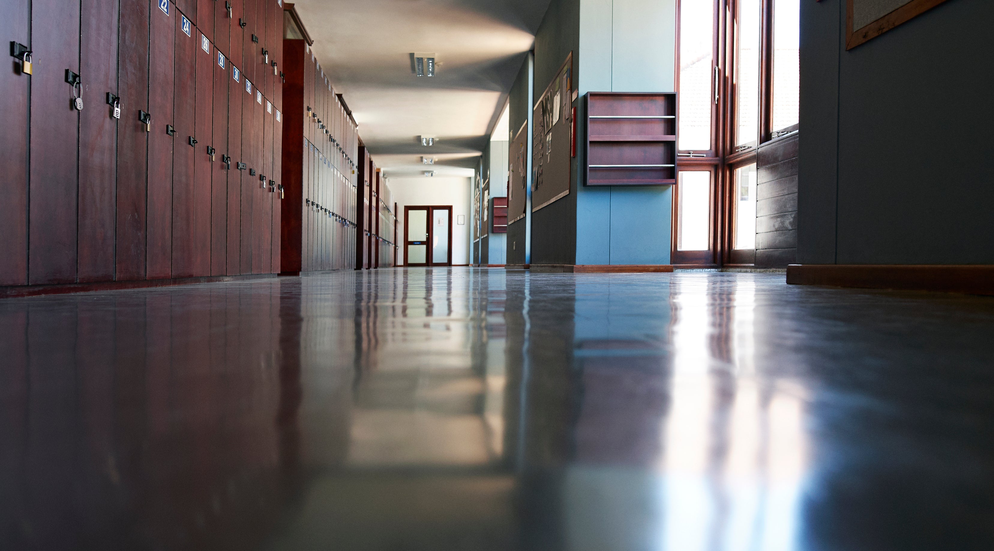 Empty school hallway with rows of lockers and windows on each side