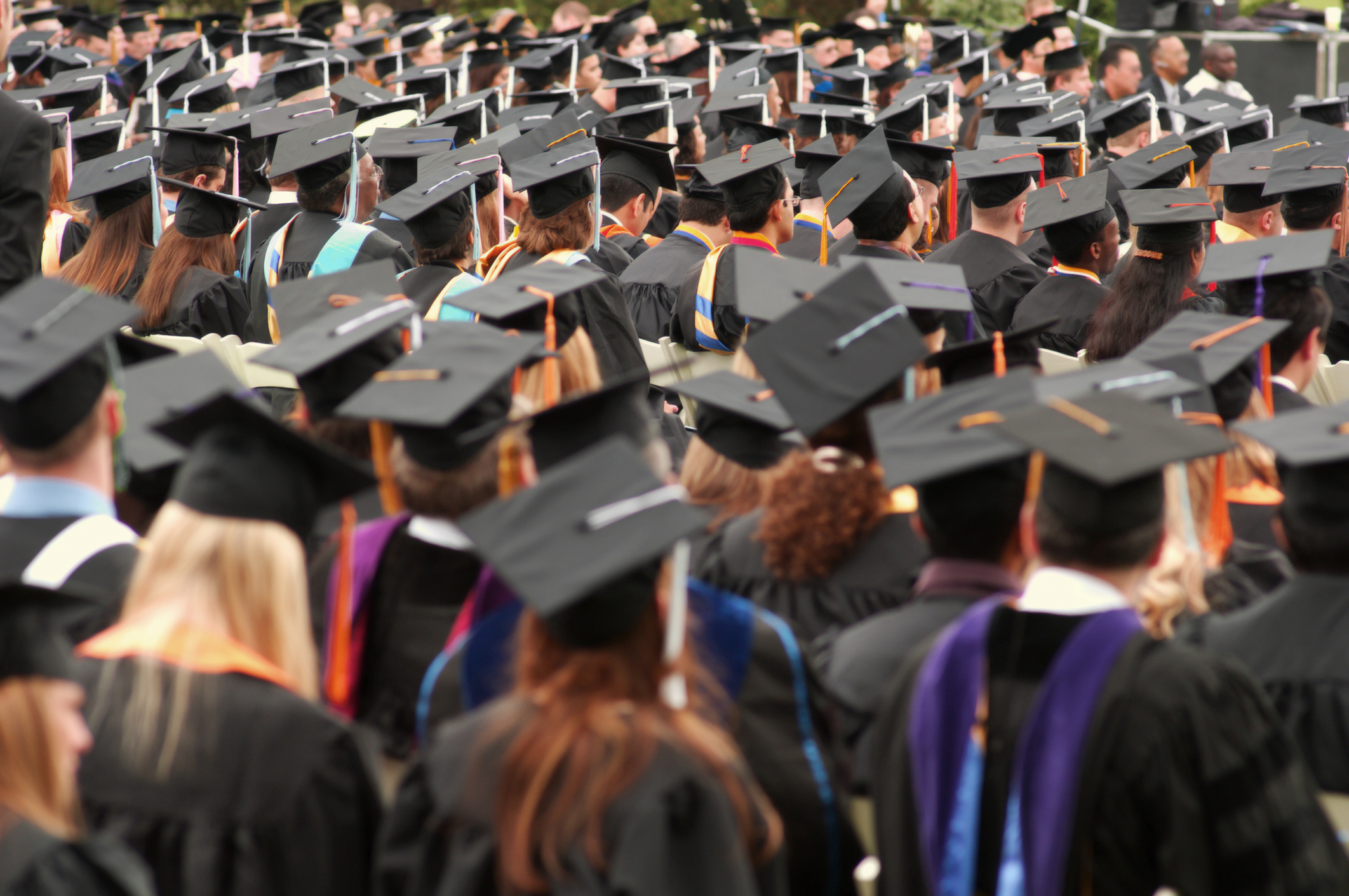 A large crowd of graduates in caps and gowns sit during a commencement ceremony, facing forward