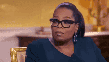 Oprah Winfrey in a television interview, sitting in a studio, wearing glasses and a dark blouse with hoop earrings