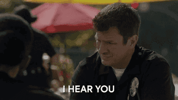 Two people in police uniforms have a conversation outdoors. Text overlay: "I HEAR YOU."