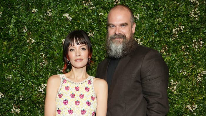Lily Allen, in a sleeveless floral dress, and David Harbour, in a dark blazer, standing in front of a greenery backdrop