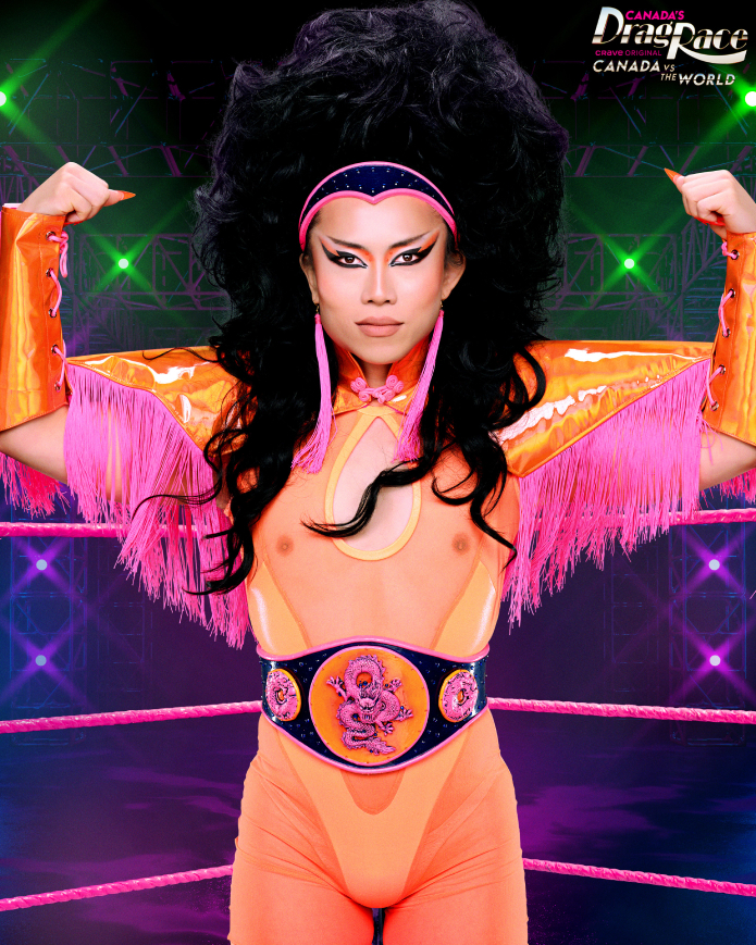 Le Fil rom Canada's Drag Race poses in a wrestling ring, flexing muscles and wearing an orange wrestling outfit with fringe and a championship belt