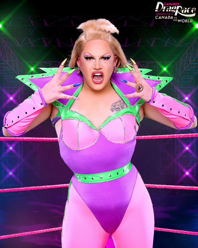 Drag queen in vibrant costume with large shoulder pads, gloves, and open-mouthed expression on "Canada's Drag Race: Canada vs. the World" stage
