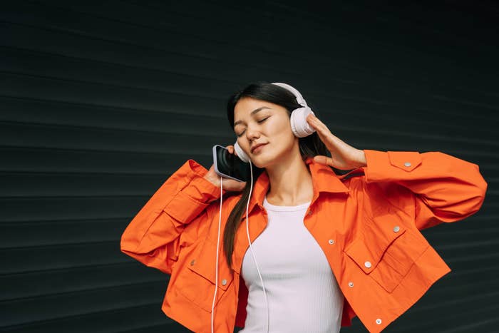 Young woman in a stylish jacket listening to music with large headphones, eyes closed, appearing relaxed and immersed in the music