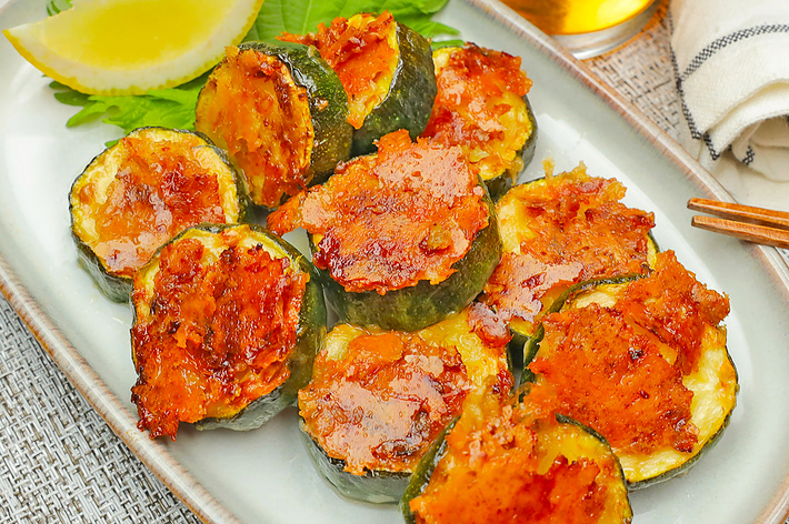 お皿に盛り付けられた焼きズッキーニチップス。トマトソースがのっている。横にはレモンのくし切りとシソの葉が添えられている。