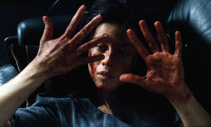Woman with bloodied hands and face lying on a chair, looking distressed