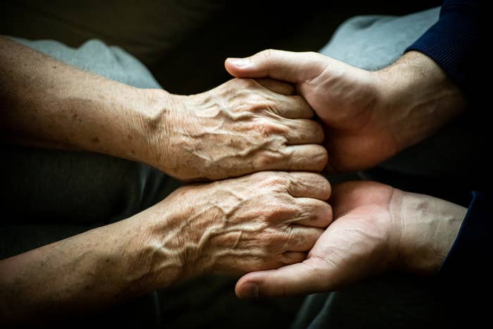 Older hands being gently held by younger hands, showing a moment of care and connection