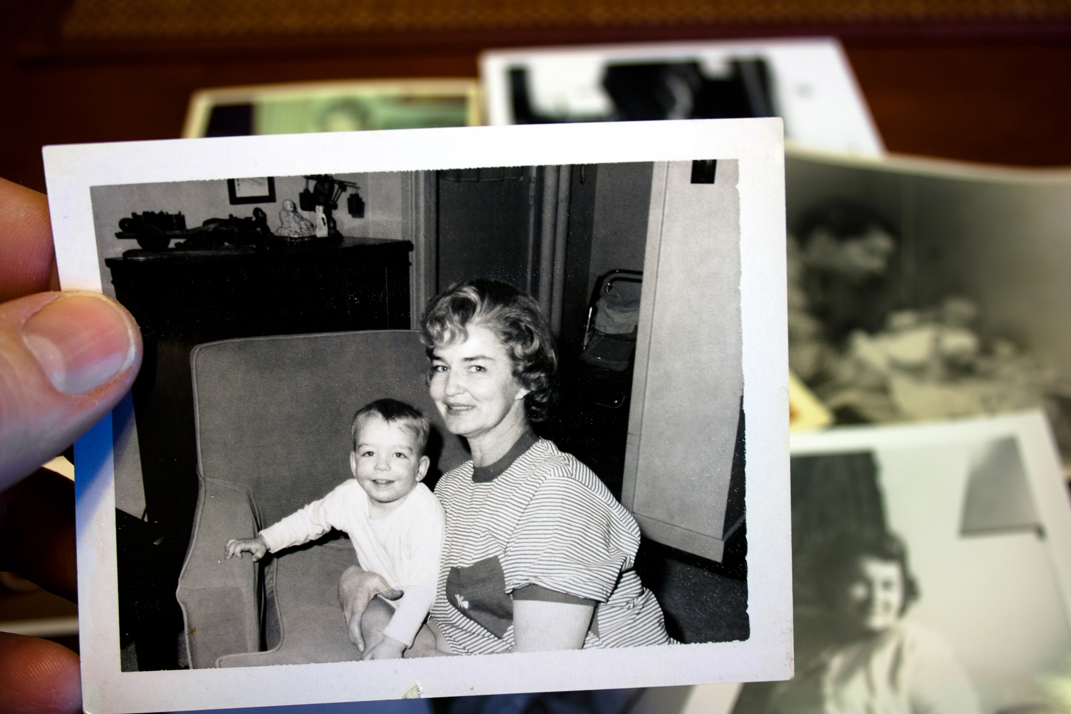 A black-and-white photo shows a woman holding a smiling baby. Several other old photos are in the background. Names unknown