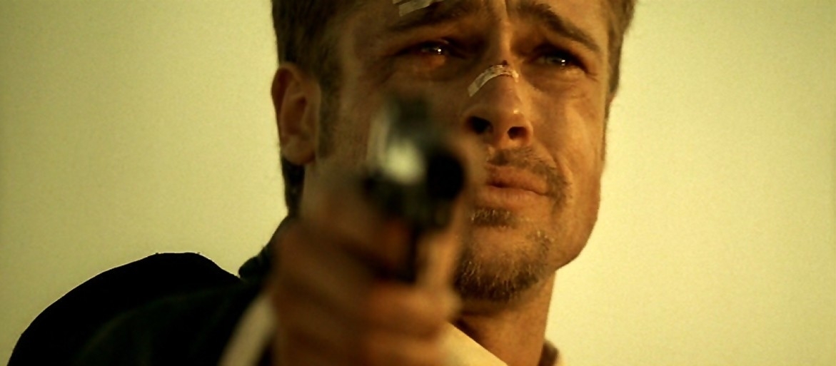 Brad Pitt, with a distressed expression and bandages on his face, points a gun in a dramatic scene from a movie
