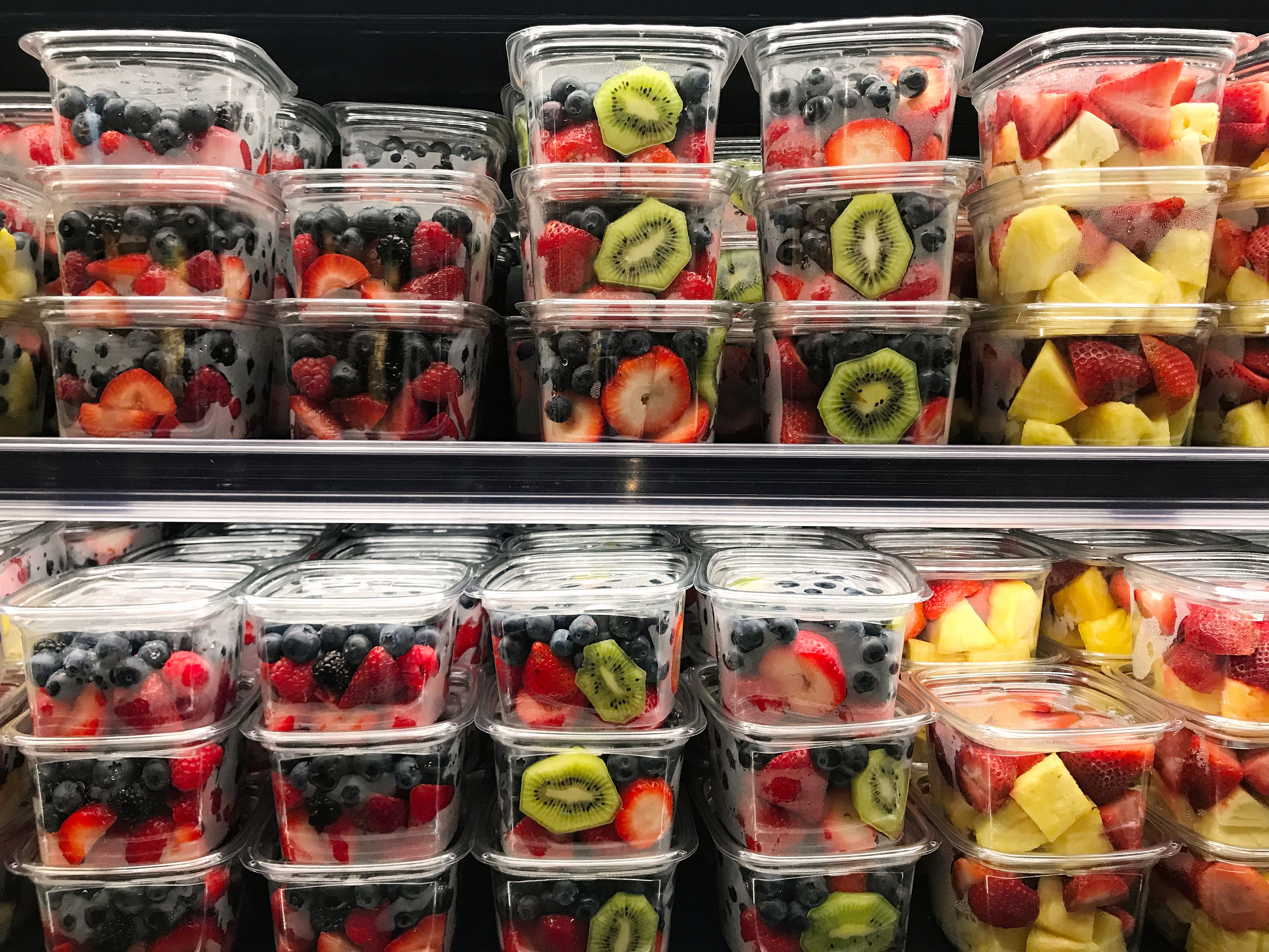 A display of pre-packaged fruit containers filled with mixed berries, kiwi slices, strawberries, and pineapple chunks