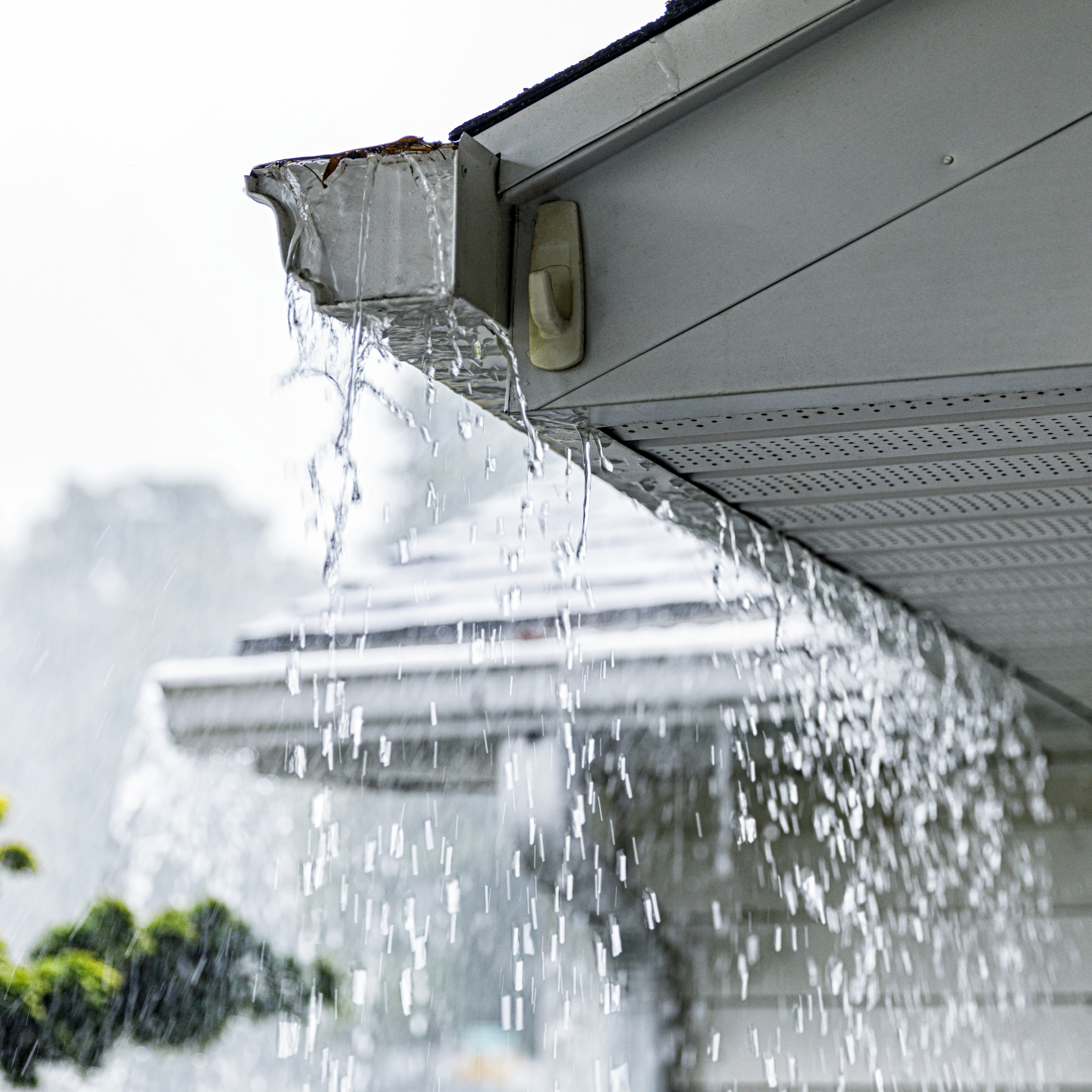 Water overflows from a clogged gutter during heavy rainfall, cascading down the side of a house's roof