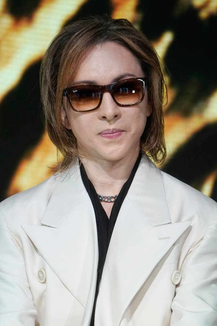 サングラスを着用し、白いジャケットを着た人物の近距離写真。背景はぼかされている。