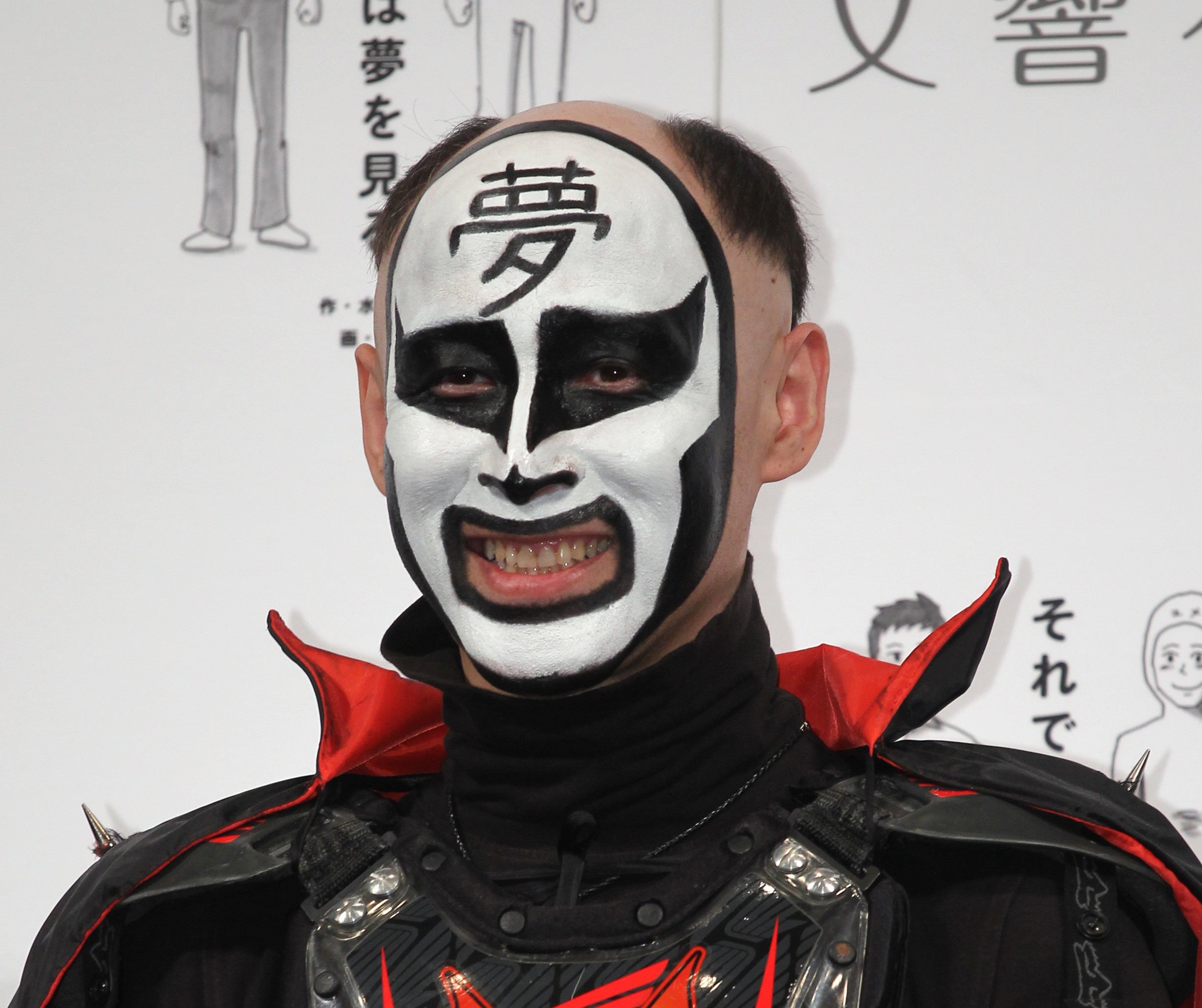 プロレスラーのグレート・ムタが黒と赤のアーマーを着て、顔に特徴的なペイントを施している。