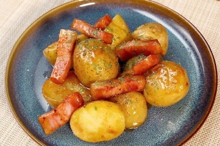 青い皿に盛られた、小さなじゃがいもとベーコンの料理。