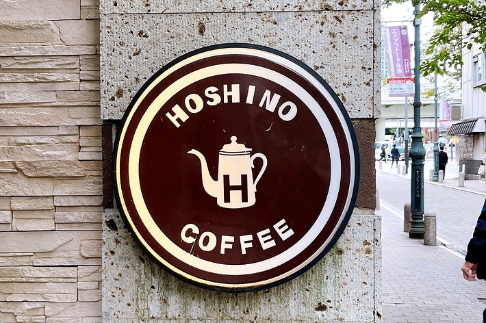 レンガの壁に掲示された「Hoshino Coffee」のサイン。交差点が背景に見える。