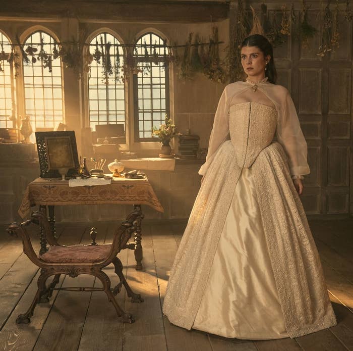 Anya Chalotra en un set con temática medieval, usando un vestido de época elegante con corpiño decorado y mangas transparentes