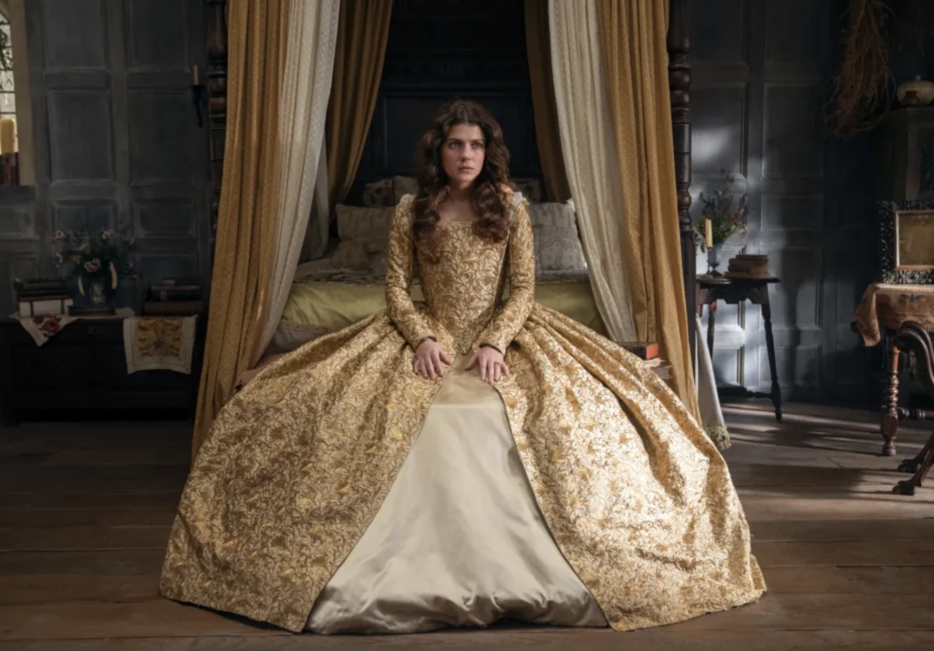 Imagen de Millie Alcock en un set de filmación, luciendo un vestido de época de estilo renacentista sentada en una habitación decorada con muebles antiguos