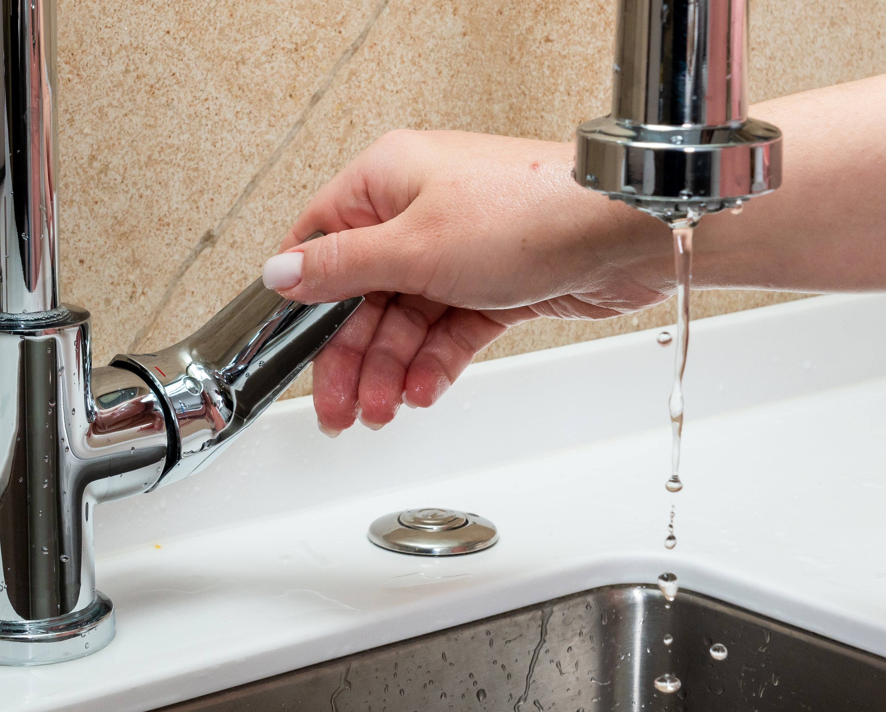 A hand turning off a chrome faucet with water droplets falling into a kitchen sink