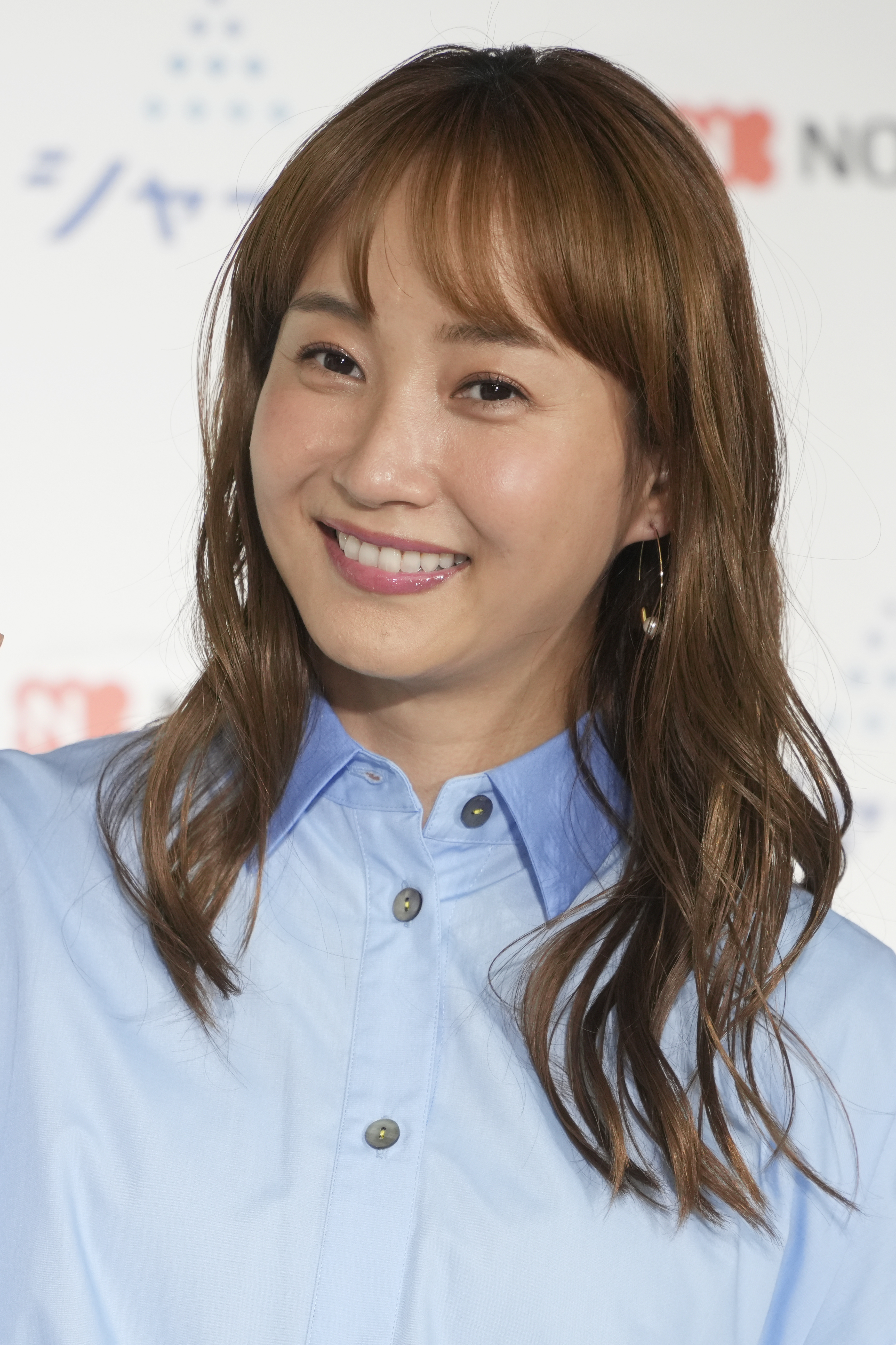 女性がカメラに向かって微笑んでいる。背景には広告が貼られています。