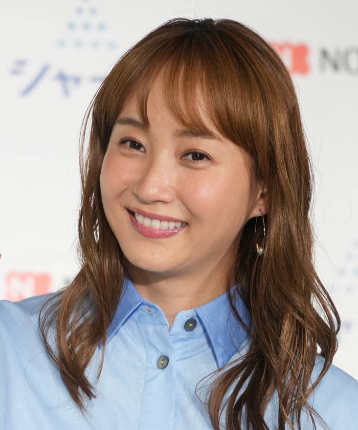 女性がカメラに向かって微笑んでいる。背景には広告が貼られています。