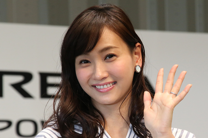 女性がカメラに向かって笑顔で手を振っている。名前は不明。